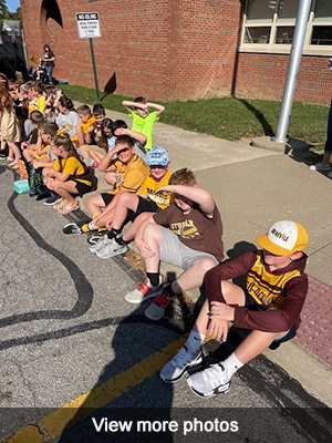Children sitting on curb outside watching homecoming - view more photos