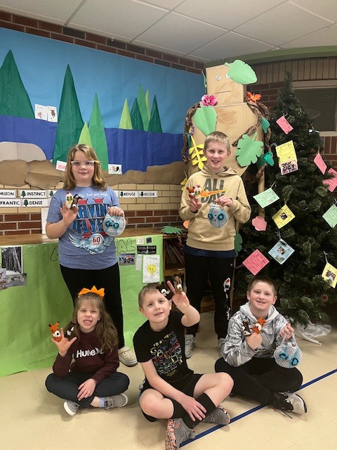 Group of happy students holding up puppets next to a Christmas tree