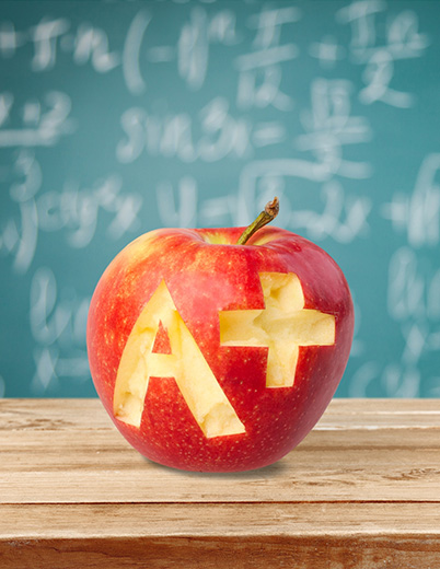 Red apple with A+ carved in it on a wooden desk